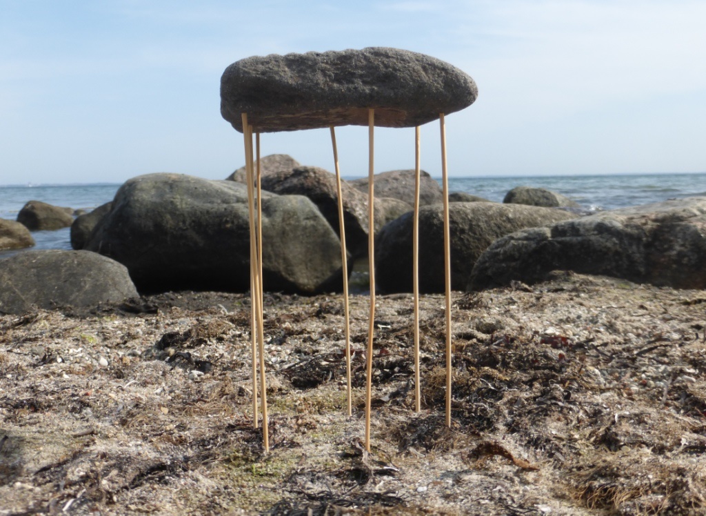 Skulptur am Strand mit Stein auf Stelzen