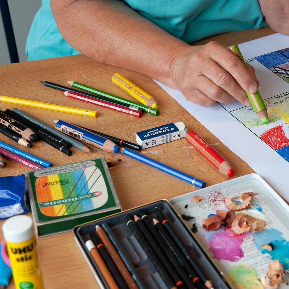 Das Bild zeigt eine Hand, die mit einem Farbstift an einer Bildfolge arbeitet. Material wie Klebestift, Farbstifte