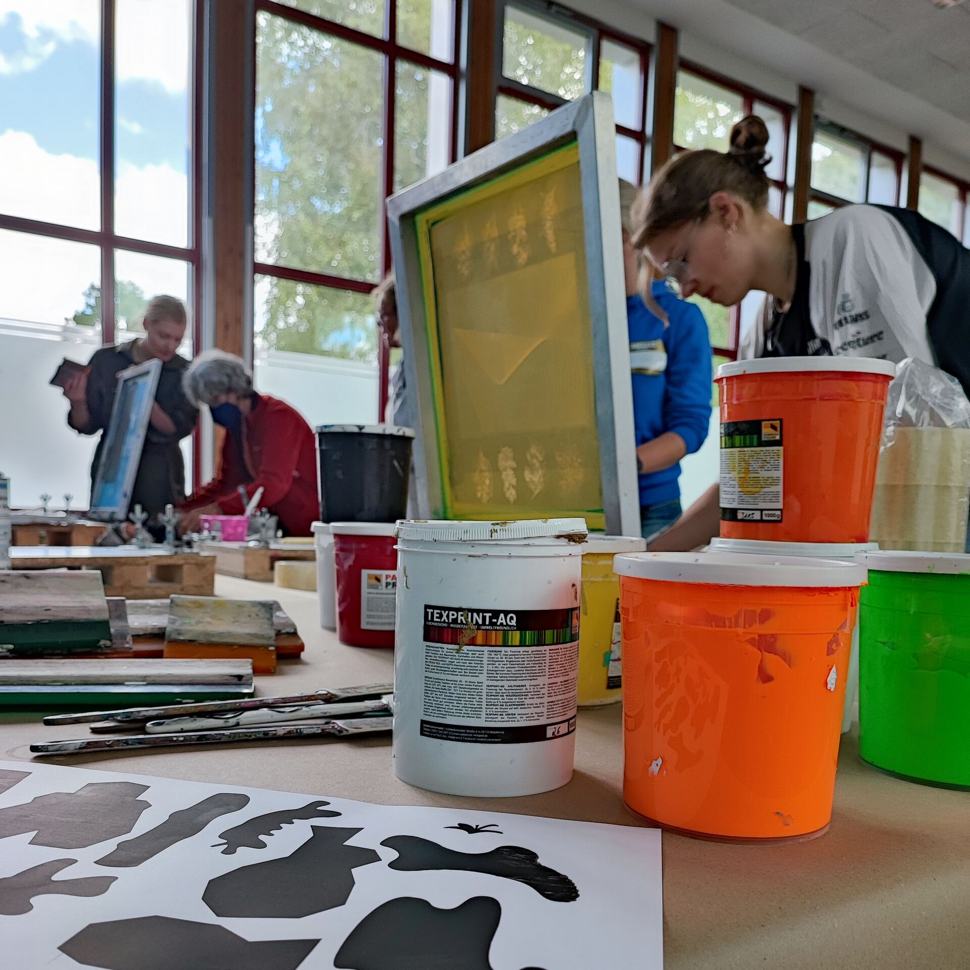 Siebdruck-Atelier mit Farbdosen und Sieben und Leuten