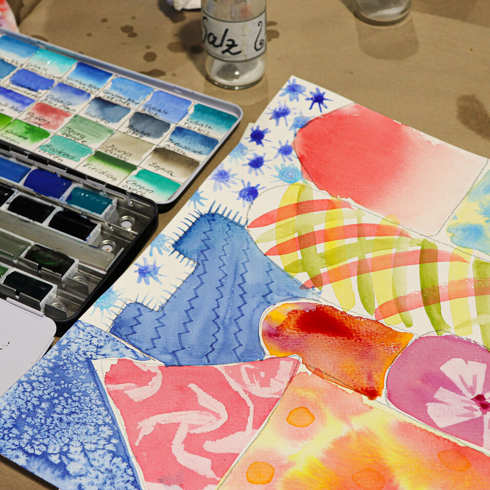 Ein Arbeitsplatz mit einem bunten Aquarell und einem Aquarell-Kasten.