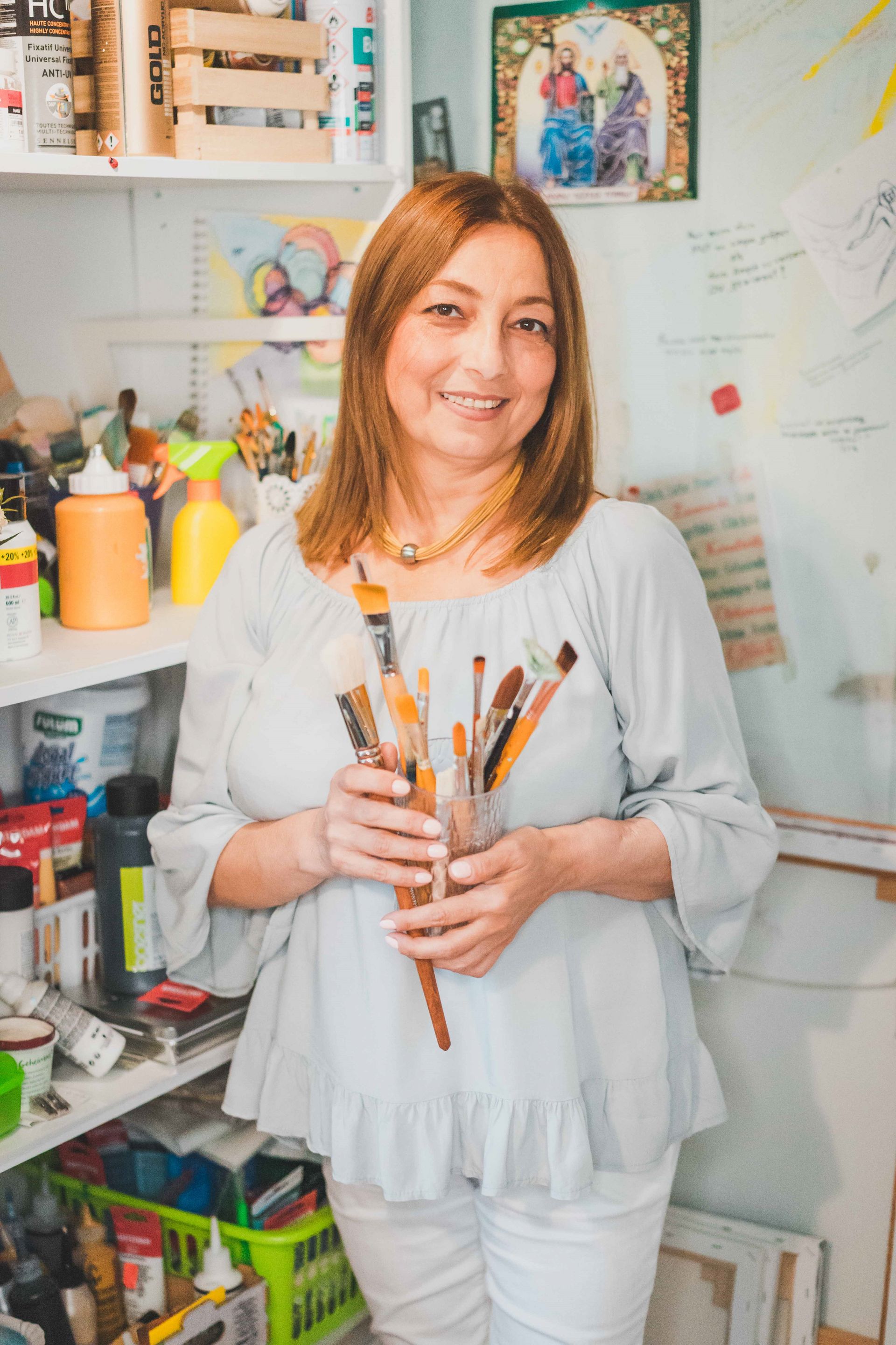 Das Bild zeigt Nora Block in ihrem Atelier mit Farben im Hintergrund und Pinsel in der Hand