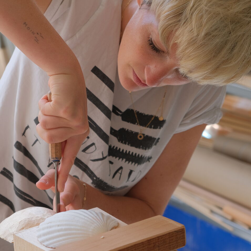 Das Bild zeigt eine Person, die eine Muschel schnitzt.