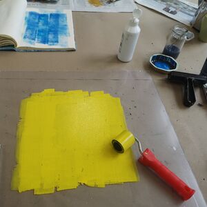 Holzschnitt-Farbe Gelb und Rolle zum Abrollen zudem ein aufgeschlagenes Buch mit blauem Holzschnitt abgebildet.