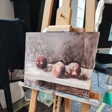 auf einer Staffelei steht eine Leinwand mit einem Apfel-Stillleben in Öl